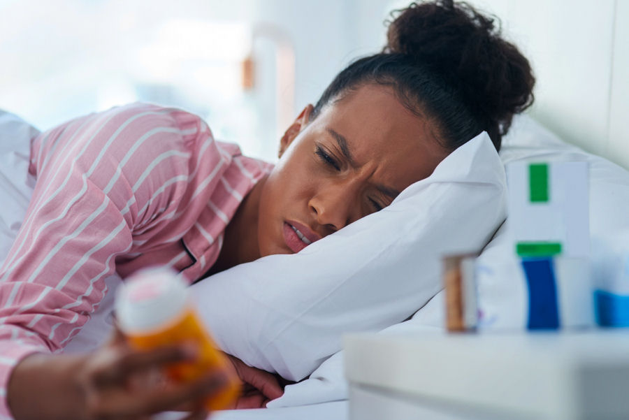 a-woman-looking-at-a-pill-bottle-laying-in-bed