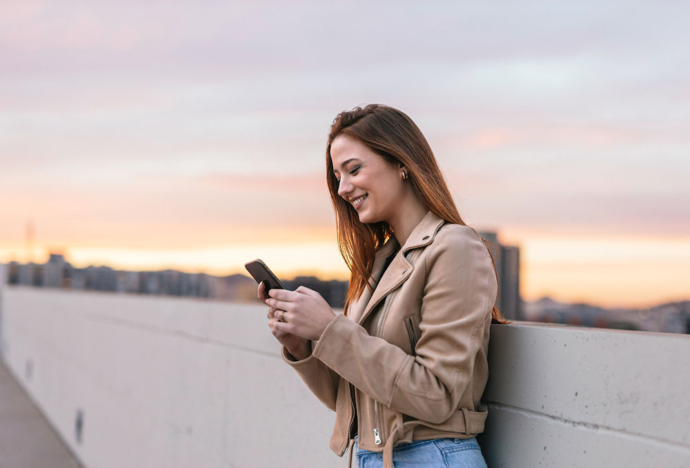 a woman smiling at cell phone leaning outside